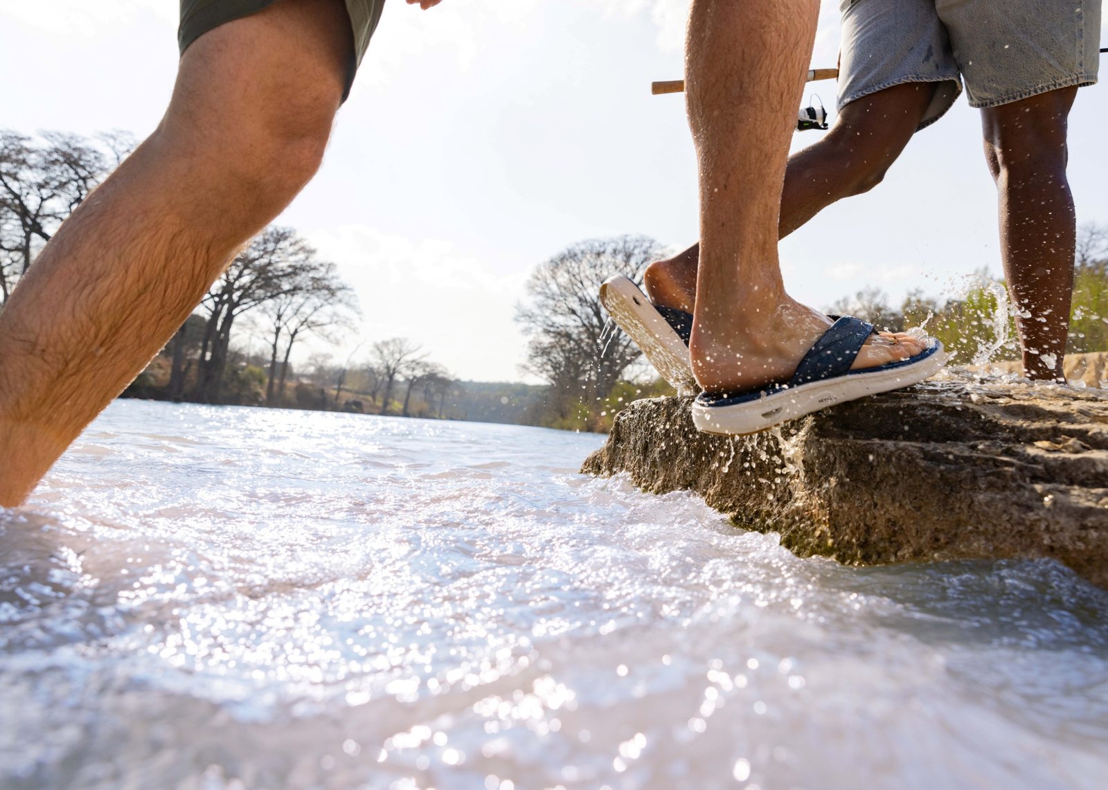 Two people stepping across wet rocks in HEYDUDE sandals